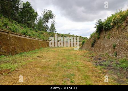 Ampia vista del fossato asciutto del forte Owcza Góra a Kłodzko, Polonia, circondato da muretti di pietra e vegetazione Foto Stock