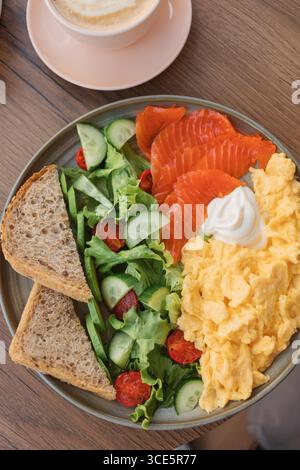 Vista dall'alto di uova strapazzate, salmone affumicato, insalata mista, pane multigrano e formaggio spalmabile con caffè latte Foto Stock