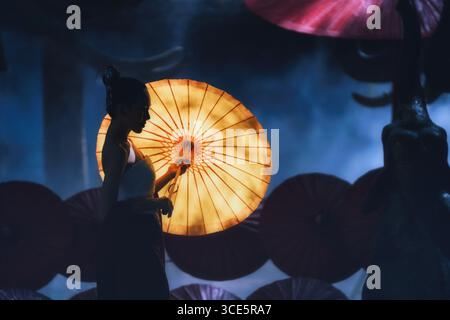 Vista laterale di una giovane donna in tradizionale abbigliamento tailandese Lanna con un ombrellone di bambù fatto a mano, Thailandia Foto Stock