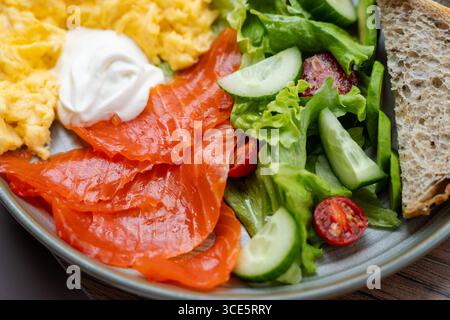 Primo piano di un piatto di salmone affumicato con uova strapazzate, insalata e pane affettato Foto Stock