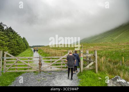 Persone trekking sul sentiero di ghiaia nella foresta Gortarowey area ricreativa con Benbulbin avvolte in nubi sulla destra, nella contea di Sligo, Connacht, Irlanda Foto Stock