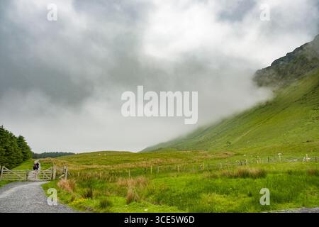 Persone trekking sul sentiero di ghiaia nella foresta Gortarowey area ricreativa con Benbulbin avvolte in nubi sulla destra, nella contea di Sligo, Connacht, Irlanda Foto Stock