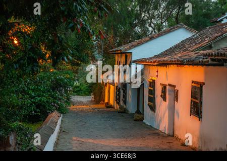 Una pittoresca vista di una strada acciottolata a Villa de Leyva, Boyaca, che mostra tradizionali case bianche illuminate da una luce calda. Foto Stock