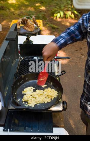 L'uomo per la cottura delle uova strapazzate in una ghisa padella su un propano camp stufa, Humbug Campeggio, Willamette National Forest, Marion County, Oregon, USA Foto Stock