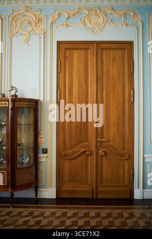 Porte doppie ornate in legno con intricati dettagli intagliati che si aprono chiusi in un'elegante camera con modanatura decorativa su pareti blu pastello e pavimento in parquet a motivi geometrici visibile Foto Stock