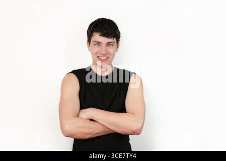 Un uomo sicuro di sé con un atteggiamento casual e un sorriso amichevole che indossa una camicia nera su sfondo bianco, sottolineando la sicurezza e la positività Foto Stock