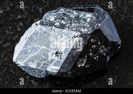 Assaggio di cristallo di granato nero melanite andradite grezzo su sfondo di granito nero da vicino dal Kazakistan Foto Stock