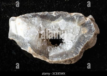 campione di strato grezzo di geode riempito di quarzo su sfondo di granito nero in primo piano Foto Stock