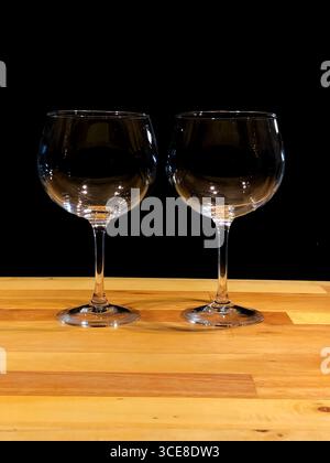Due bicchieri da vino vuoti su un tavolo di legno con sfondo scuro Foto Stock