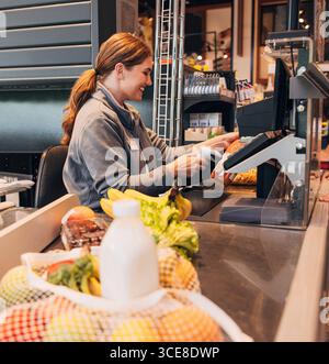 Giovane donna che lavora come cassiera in un negozio di alimentari scansionando una bottiglia di succo giovane donna che lavora come cassiera in un negozio di alimentari scansionando una bottiglia Foto Stock