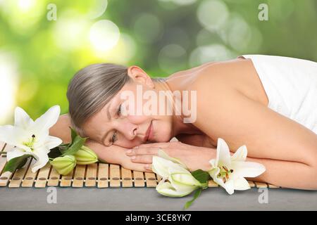 Bella donna che si rilassa su un tappeto di bambù su sfondo verde sfocato. Centro benessere Foto Stock