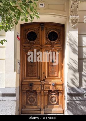Una porta di legno splendidamente intagliata con motivi intricati e inserti in ferro battuto sotto una targa numero edificio in un ingresso illuminato dal sole Foto Stock
