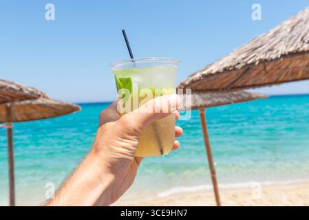 Cocktail rinfrescante con lime e menta sullo sfondo di una spiaggia tropicale, perfetto per vacanze estive e vacanze Foto Stock