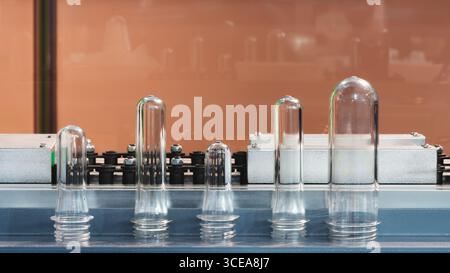 Preforme in plastica PETG per la produzione di bottiglie sul nastro trasportatore prima della pressa per soffiaggio a caldo Foto Stock