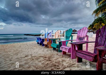 Colorate sedie Adirondack allineate lungo una spiaggia di Aruba Foto Stock