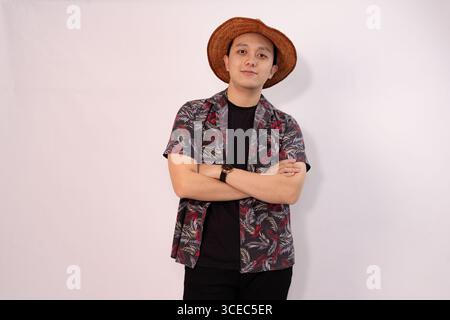 giovane casual che posa con le braccia incrociate e indossa un cappello di paglia Foto Stock