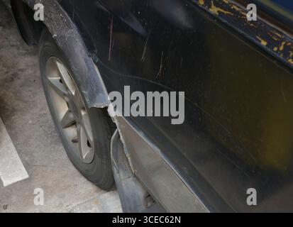 Primo piano parafango danneggiato di una vecchia auto nel parcheggio Foto Stock