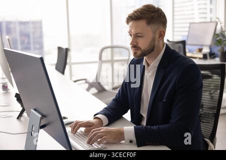 Un giovane commerciante serio e impegnato seduto sul desktop Foto Stock