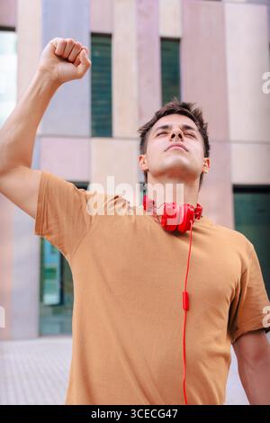 Giovane felice che solleva pugno per festeggiare indossando le cuffie rosse all'aperto Foto Stock