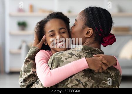 Amorevole madre nera in uniforme militare baciare figlia Foto Stock