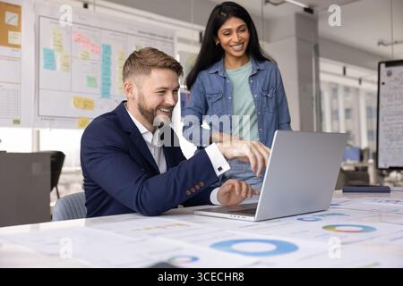 Coppia multietnica di allegri colleghi d'affari che utilizzano un notebook Foto Stock