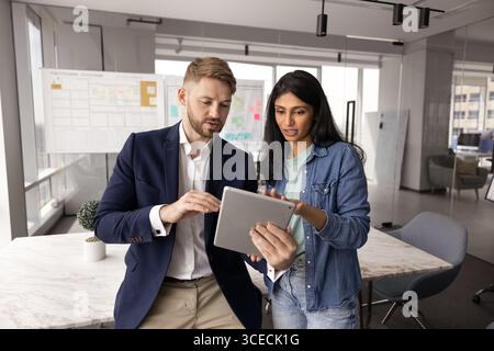 Giovane uomo d'affari caucasico che mostra tablet a una collega indiana Foto Stock