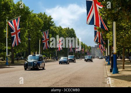Londra, Inghilterra - London Taxis supera i Many Union Jacks che fiancheggiano il Mall guardando verso Buckingham Palace nel centro di Londra. Foto Stock