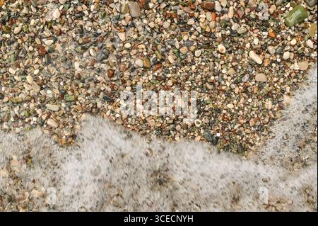 vista della costa di ciottoli con delicata schiuma marina. Colorati ciottoli di mare sparsi lungo la costa, con le onde che si lavano delicatamente sopra di loro. beac multicolore Foto Stock