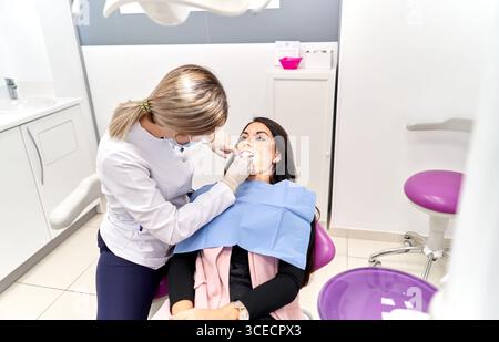 Un dentista sta sta esaminando un paziente in una moderna clinica odontoiatrica. Il paziente è seduto su una sedia reclinabile mentre indossa un bavaglino protettivo. L'impostazione è Foto Stock