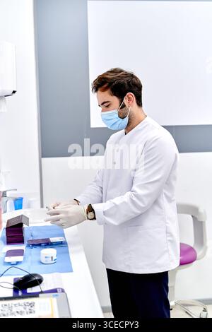 Un operatore sanitario in ambiente medico indossa guanti in lattice, garantendo igiene e sicurezza. Il medico è concentrato, indossa una maschera e si prepara Foto Stock