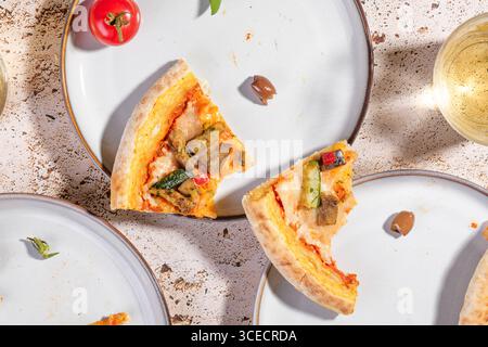 Vista dall'alto delle fette di pizza vegetariana su un piatto bianco con zucchine, melanzane e peperoni. Accompagnato da olive e pomodoro ciliegino Foto Stock