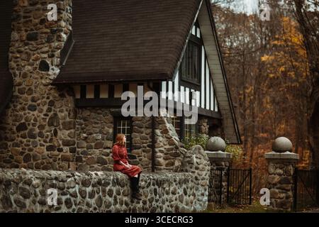 Una donna siede in un rustico cottage in pietra nella campagna del Quebec, circondato dai caldi colori dell'autunno. La scena cattura l'essenza della pace Foto Stock