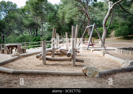 Un tranquillo parco nascosto nella foresta durante il pomeriggio, con un parco giochi in legno. L'ambiente tranquillo e' circondato da alti alberi e naturale Foto Stock