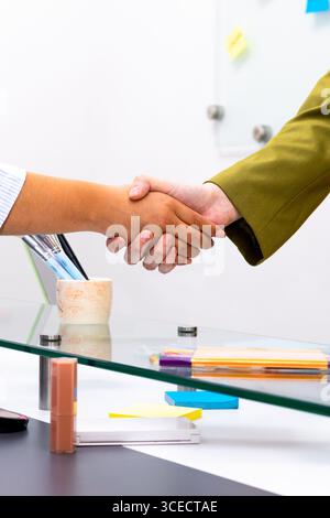 Primo piano di una stretta di mano tra due professionisti su un tavolo di vetro, che simboleggia il successo di una negoziazione o di una partnership, in un ambiente di ufficio moderno Foto Stock