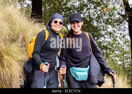 Una coppia allegra di escursionisti fa una pausa su un sentiero panoramico nella foresta. Indossati con outfit per esterni e zaini da trasporto, incarnano lo spirito dell'avventura A. Foto Stock