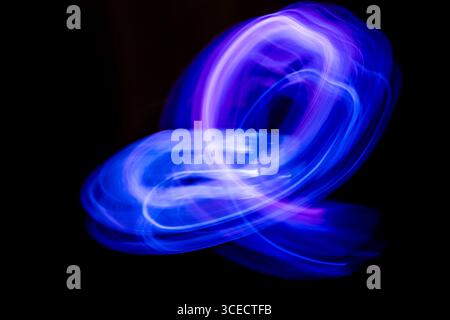 Un'accattivante immagine astratta con vorticose tracce di luci al neon blu e viola. La tecnica della fotografia a lunga esposizione crea uno shap dinamico e fluido Foto Stock