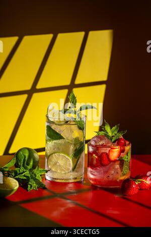 Rinfrescanti cocktail mojito esposti su un vivace tavolo. Un classico mojito con lime e menta e un mojito di fragole con fragole fresche. B Foto Stock