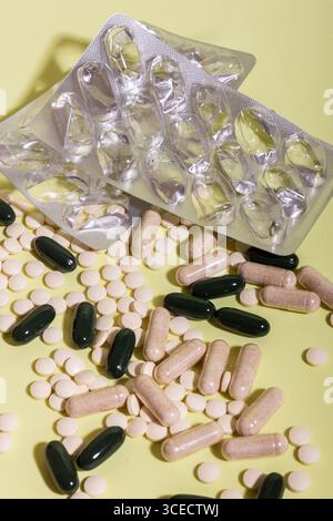 Una collezione di pillole e capsule assortite sparse su una superficie gialla accanto alla confezione vuota in blister, che mostra diversi tipi di farmaci per la guarigione Foto Stock