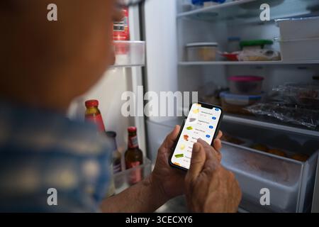 Uomo anziano ritagliato irriconoscibile che utilizza uno smartphone per acquistare generi alimentari online, sfogliando un'app digitale per i prodotti mentre si trova di fronte a un Foto Stock