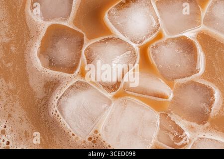 Una vista dettagliata dall'alto verso il basso del caffè freddo ghiacciato, che mostra cubetti di ghiaccio che galleggiano nell'estrazione. Il caffè marrone chiaro contrasta con la nitidezza di Foto Stock