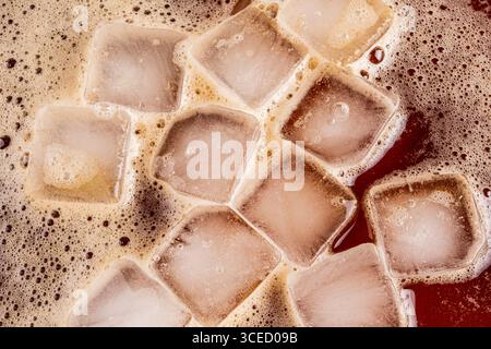 Un'immagine ravvicinata del caffè ghiacciato con cubetti di ghiaccio fluttuanti. I cubetti di ghiaccio creano un rinfrescante contrasto visivo con il caffè marrone scuro, offeri Foto Stock