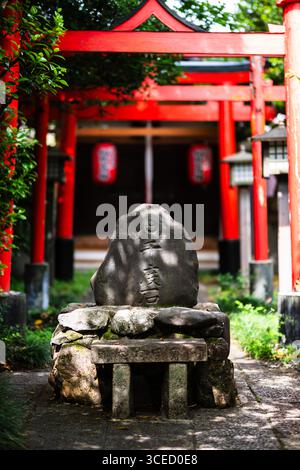Un tranquillo cartello in pietra si trova sotto una vivace porta rossa a Daihōonji, il tempio Senbon Shakadō a Kyoto, in Giappone, circondato da una vegetazione lussureggiante e da un tradizionale a Foto Stock