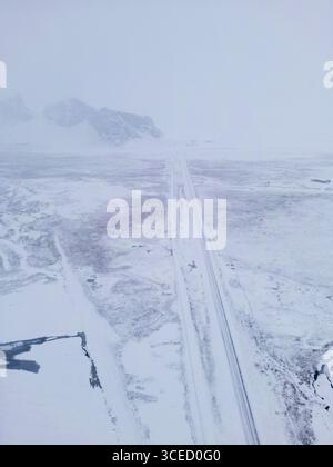 Vista aerea di un remoto paesaggio invernale islandese, che mostra vaste distese di terreno innevato e una lunga strada ghiacciata che taglia attraverso la natura selvaggia e. Foto Stock