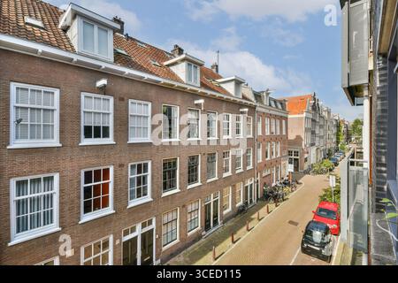 Una vista pittoresca di una strada residenziale di Amsterdam caratterizzata da un'architettura classica, fiancheggiata da biciclette e auto parcheggiate sotto un cielo azzurro. Foto Stock