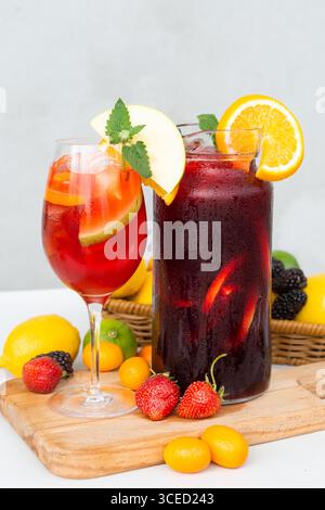 Due rinfrescanti sangrias estive con frutta vibrante. Un bicchiere e una caraffa riempite di fette colorate di arancia, mela e foglie di menta. Impostare su A. Foto Stock