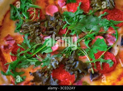 Un succulento primo piano di una pizza condita con rucola fresca e verdi vivaci, accentuati da fette di peperoni e formaggio fuso, creando un colle Foto Stock