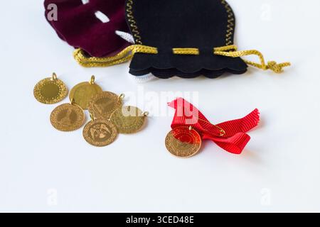 Monete tradizionali in oro turco con nastro rosso e sacchetti in oro velluto su superficie bianca Foto Stock