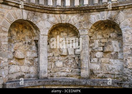 Le pareti in pietra intemprata presentano tre archi distinti all'interno di un'antica struttura, che mostrano texture ruvide e una ricca storia sotto il caldo bagliore Foto Stock