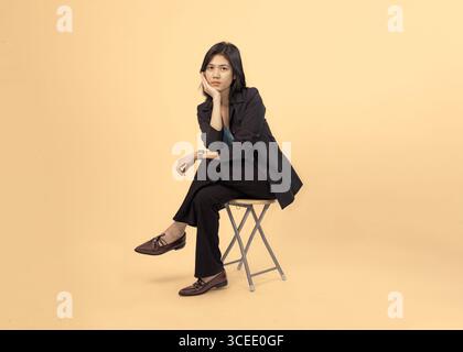 donna professionista in tuta nera che posa con sicurezza su un solido sfondo beige Foto Stock