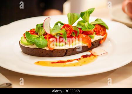 Un vibrante panino a faccia aperta presenta una base di pane scuro ricoperto da crema spalmabile, peperoni colorati, pomodori e verdure fresche. Mi sono divertito in un hotel Foto Stock